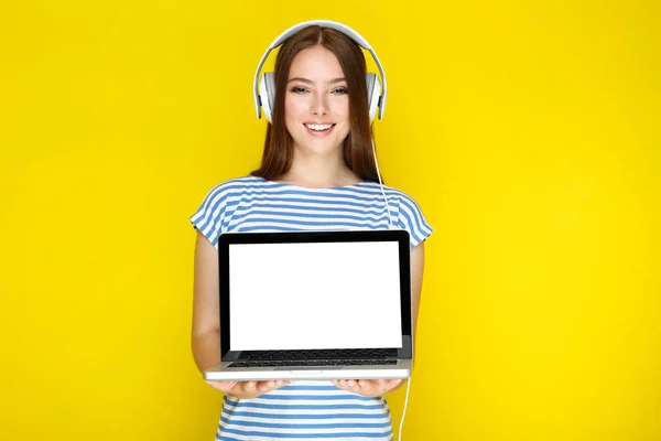 Jonge vrouw in hoofdtelefoon toont lege laptop scherm op geel — Stockfoto