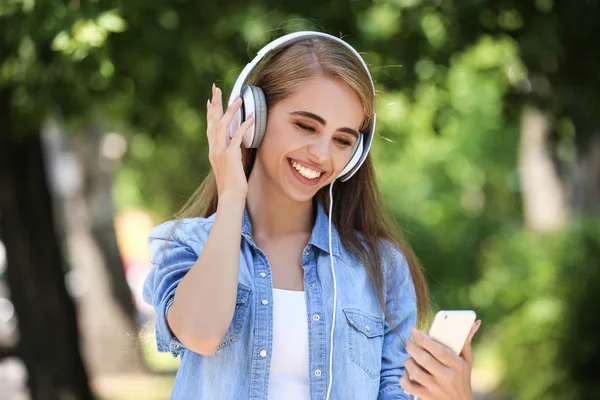 Mladá usměvavá dívka poslech hudby se sluchátky a pomocí sma — Stock fotografie