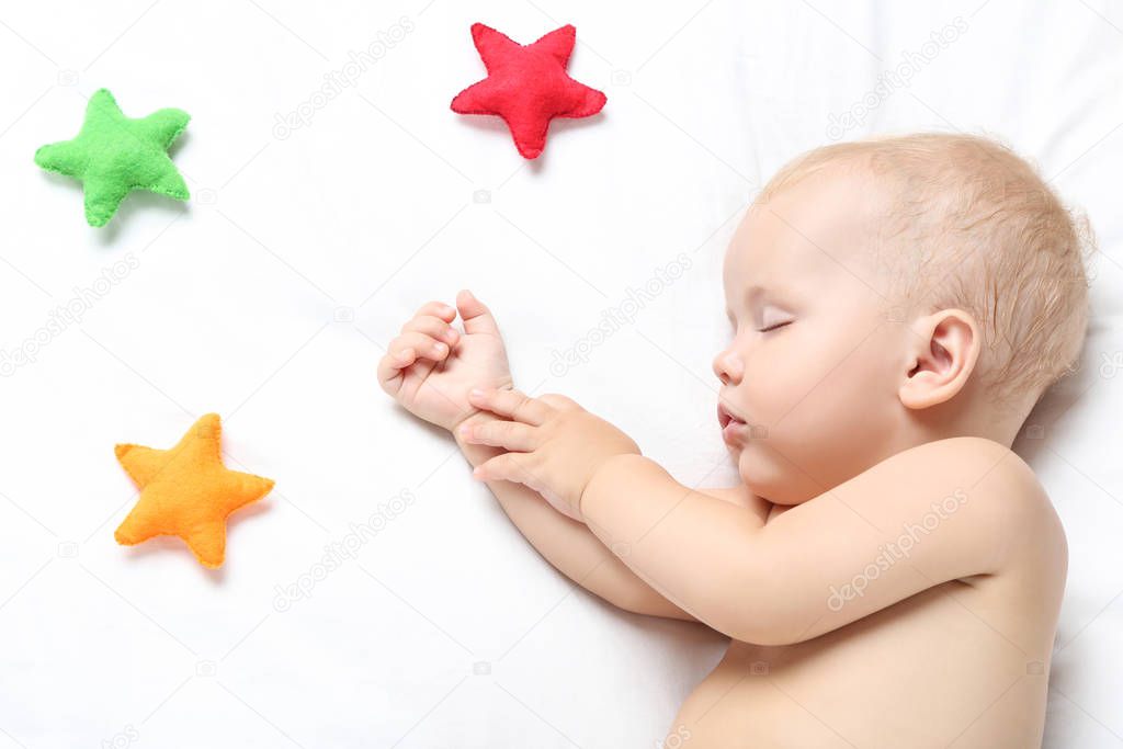 Beautiful little boy sleeping on bed at home with colorful fabri