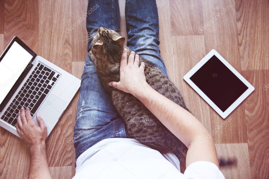 Man sitting on the floor with tablet computer, laptop and beautiful cat
