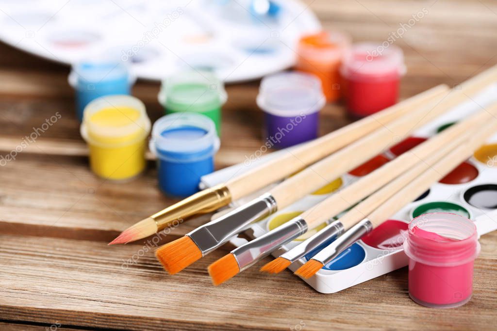 Colorful gouache paints and brushes on brown wooden table