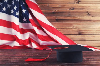 Kahverengi ahşap masada Amerikan bayrağı olan mezuniyet şapkası.