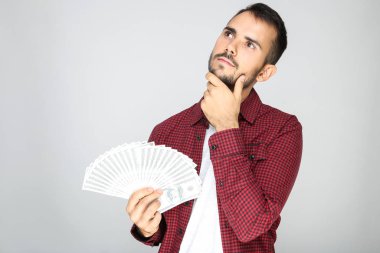 Gri arka planda dolar banknotları tutan genç adam.
