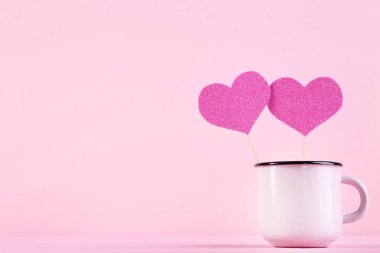 Pembe arka planda kupası olan kağıt kalpler.