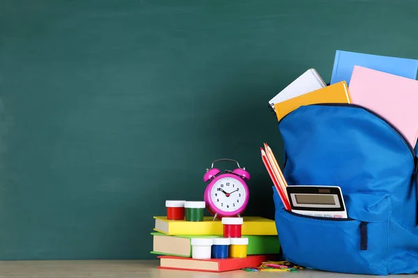 Material escolar con mochila azul sobre fondo pizarra —  Fotos de Stock