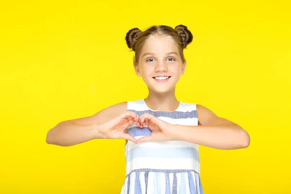 Menina bonita nova mostrando coração por mãos no fundo amarelo — Fotografia de Stock