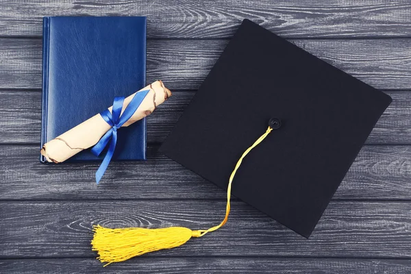 Tapa de graduación con diploma y bloc de notas sobre mesa de madera negra — Foto de Stock