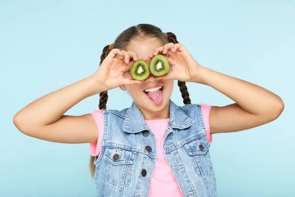 Молода дівчина прикриває очі ківі фруктами на синьому фоні — стокове фото