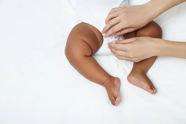 Menina americana deitada na cama branca com as mãos da mãe — Fotografia de Stock