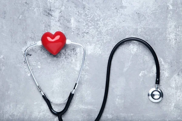 Stetoskop s červeným srdcem na šedém dřevěném stole — Stock fotografie