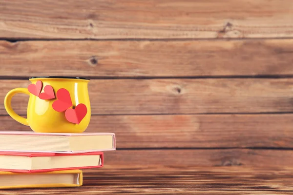 Paper hearts with yellow mug and stack of books on brown wooden