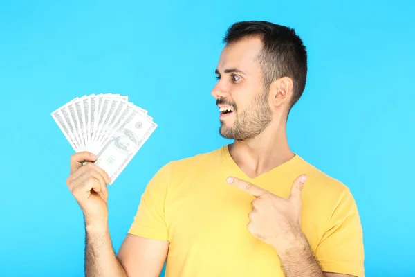 Joven hombre feliz sosteniendo billetes de dólar sobre fondo azul — Foto de Stock