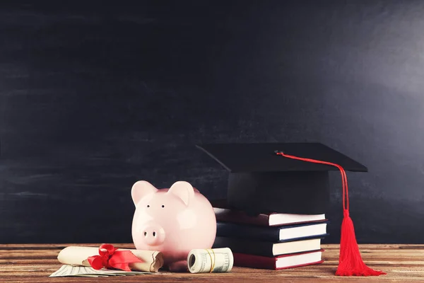 Пиггибанк с выпускной шапкой, деньгами и книгами на доске — стоковое фото