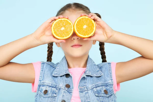 Młoda dziewczyna pokrywa oczy pomarańczowym owocem na niebieskim tle — Zdjęcie stockowe