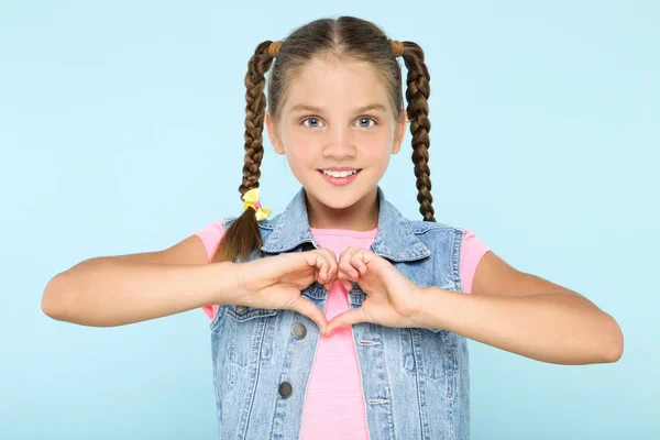 Menina bonita nova mostrando coração por mãos no fundo azul — Fotografia de Stock