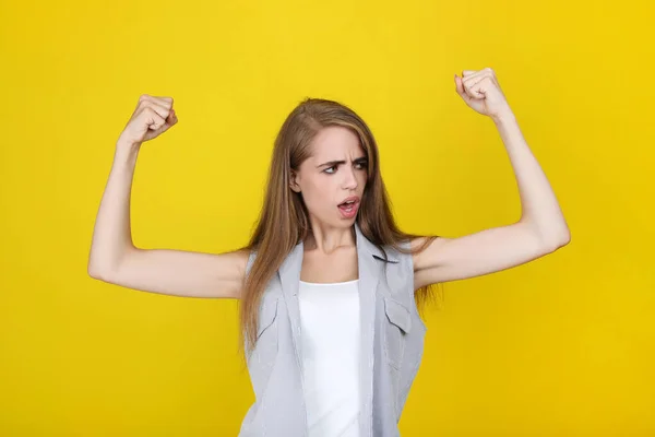 Ung vacker flicka som visar händerna muskler på gul bakgrund — Stockfoto