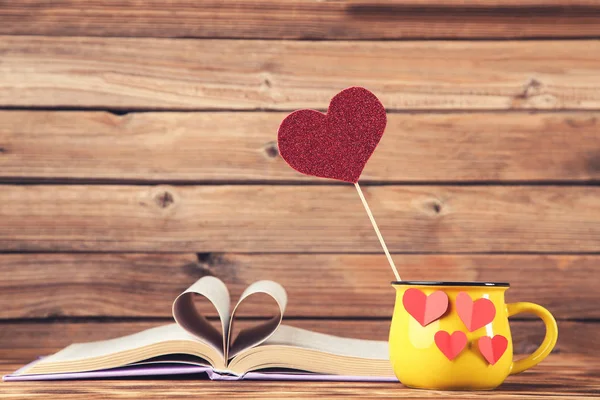 Paper hearts with yellow mug and book on brown wooden table