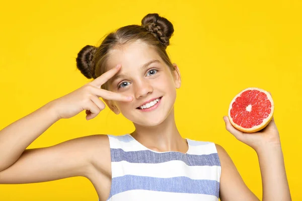 Молода дівчина тримає грейпфрут і показує два пальці на жовтому тлі — стокове фото