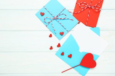 Beyaz ahşap masanın üzerinde kırmızı kalpler olan kağıt zarflar.