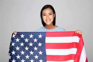 Gri arka planda Amerikan bayrağı tutan genç bir kadın.