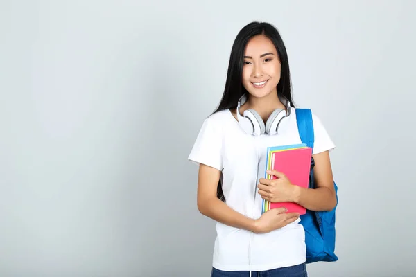 Jonge vrouw met boeken, koptelefoon en rugzak op grijze backgrou — Stockfoto