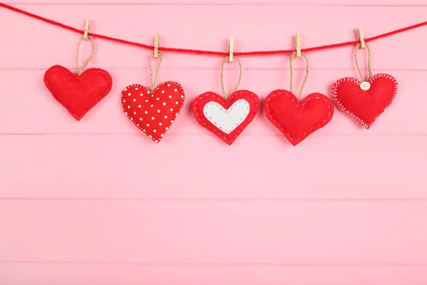 Corazones de tela con pinzas de ropa colgando sobre fondo de madera rosa —  Fotos de Stock