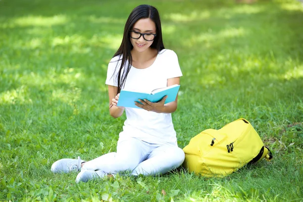 Красива молода жінка з книгою і рюкзаком сидить на зеленому gr — стокове фото