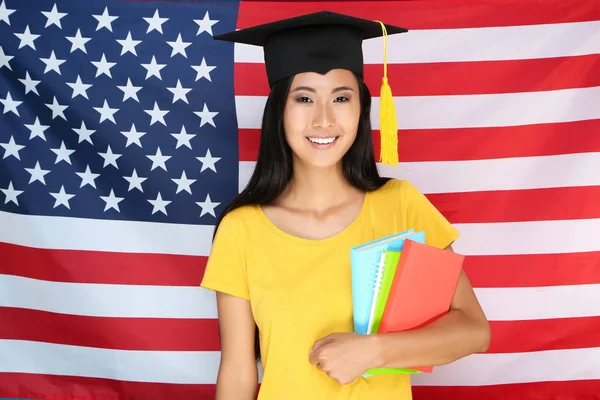 Mujer joven con gorra de graduación sosteniendo libros sobre la bandera americana bac — Foto de Stock