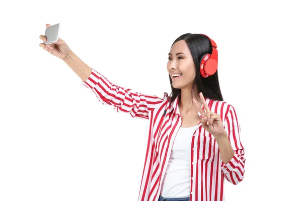 Mujer joven con auriculares haciendo selfie en el teléfono inteligente en blanco —  Fotos de Stock