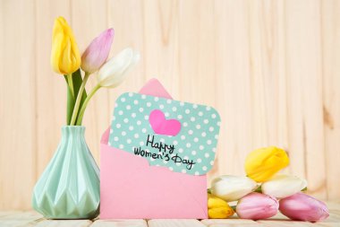 Kahverengi ahşap arka planda lale çiçekleri ve zarf ile Mutlu Kadınlar Günü 'nü yaz.