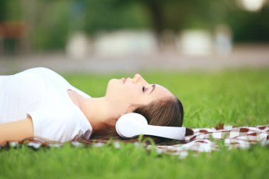 Genç mutlu kız yeşil çimenlerde uzanıyor ve kulaklıkla müzik dinliyor.