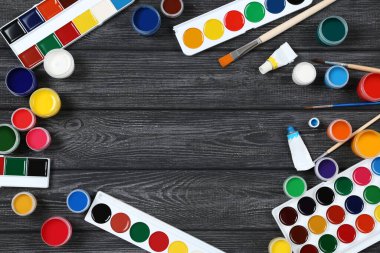 Siyah ahşap masada renkli guaj boyaları ve fırçalar.