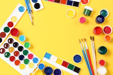 Sarı arka planda renkli guaj boyaları ve fırçalar