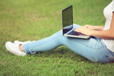 Dizüstü bilgisayarı olan genç bir kız parkta çimlerde oturuyor.