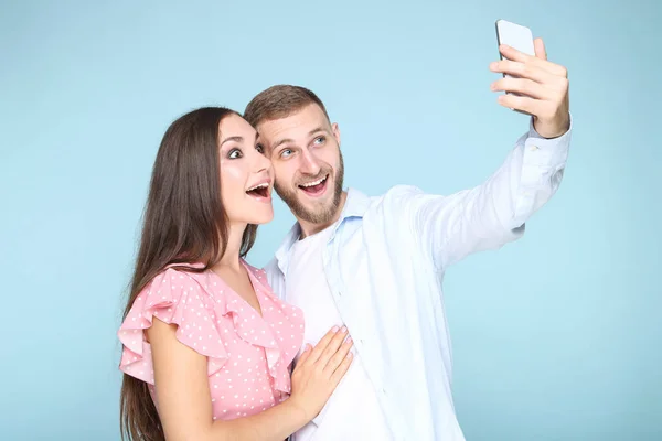 快乐的年轻夫妇在蓝色背景的智能手机上自拍 — 图库照片