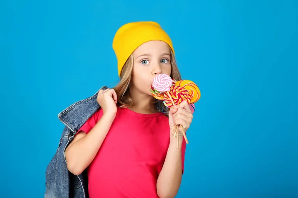 Young girl in fashion clothing with colorful lollipops on blue background