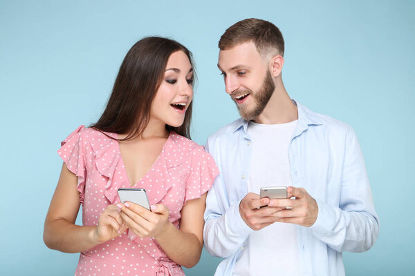 Happy young couple with mobile phones on blue background