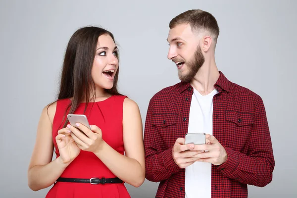 快乐的年轻夫妇 有灰色背景的手机 — 图库照片