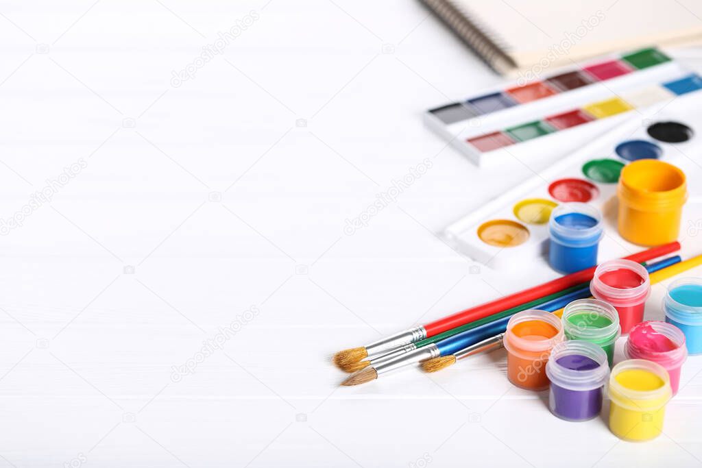 Colorful gouache paints and brushes on white wooden table