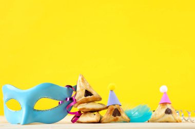 Purim tatil kompozisyonu. Sarı arka planda parti malzemeleri olan kurabiyeler.