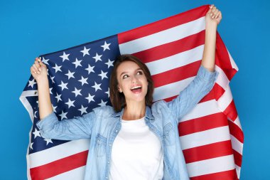 Güzel genç bir kadın mavi arka planda Amerikan bayrağını tutuyor.