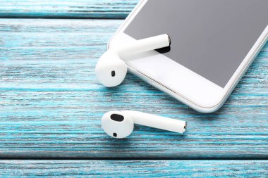 Mavi ahşap masada cep telefonu olan beyaz kablosuz kulaklıklar.