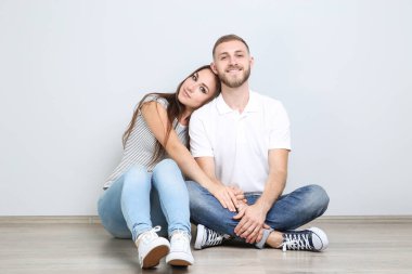 Gri arka planda yerde oturan mutlu genç çift