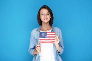 Güzel genç bir kadın mavi arka planda Amerikan bayrağını tutuyor.