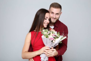 Gri arka planda bir buket çiçekli mutlu genç çift