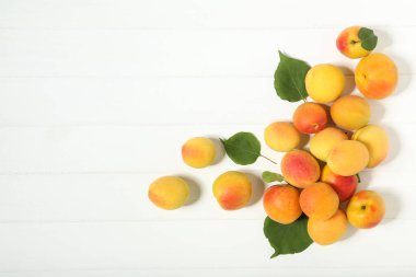 Beyaz ahşap masa üzerinde yeşil yapraklı tatlı kayısı