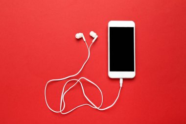 Kırmızı arka planda cep telefonu olan kulaklıklar.