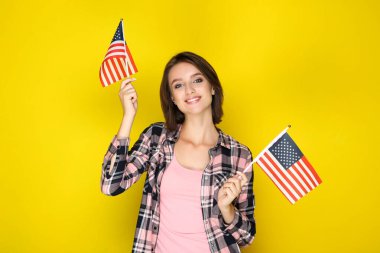 Güzel genç bir kadın sarı arka planda Amerikan bayrakları taşıyor.