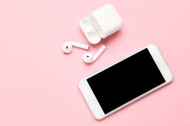Pembe arka planda cep telefonu olan beyaz kablosuz kulaklıklar.