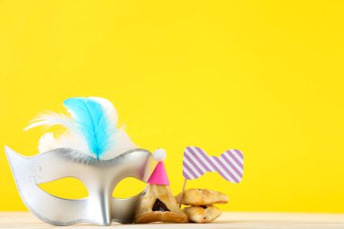 Purim tatil kompozisyonu. Sarı arka planda parti malzemeleri olan kurabiyeler.